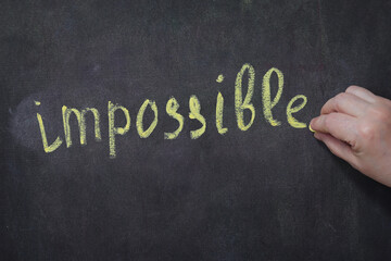 an elderly woman writes the word Impossible on the board in chalk