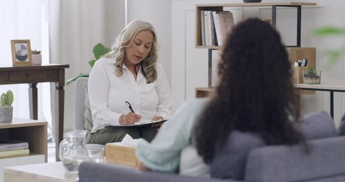 Mature female psychologist writing while listening to her patient talk about issues and problems. Young patient and her shrink during a therapy session and getting advice on balancing her emotions