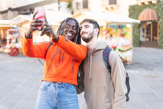 Happy multiethnic couple in the city taking photo - Smiling man and african girl taking selfie with smartphone on street – multiracial Happy couple having fun and taking a selfie – mixed race smiling 