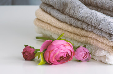 A stack of terry shower towels on a white table close-up next to artificial peony flowers.