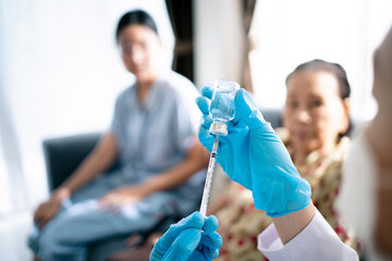 Doctor preparing a vaccine in syringe for injecting on Asian elder woman arm.