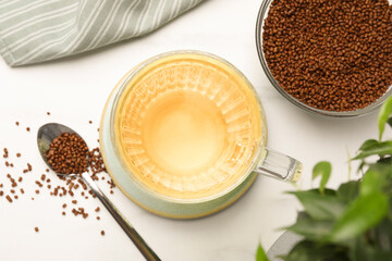 Cup of buckwheat tea and granules on white marble table, flat lay