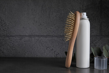 Fototapeta na wymiar Dry shampoo spray, eucalyptus branch and hairbrush on dark table near grey wall. Space for text