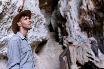 A young man wearing a hat is having fun exploring a cave and taking a look inside