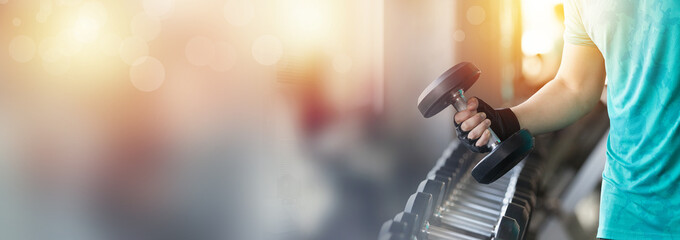 Close up of hand holding metal dumbbell from the rack in the gym. Hand of muscular man picking heavy metal dumbbell in the gym. .double exposure with bokeh, banner cover concept.