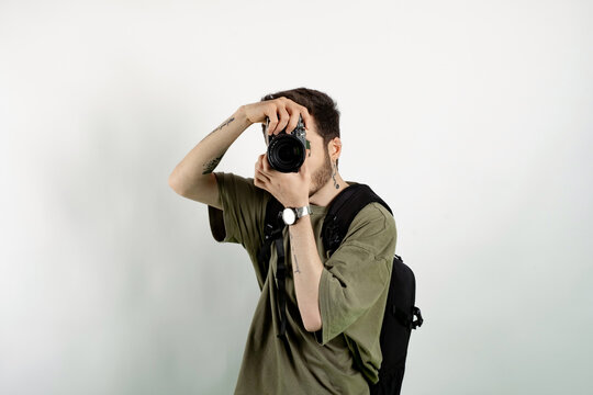 Caucasian man wearing khaki tee posing isolated over white background taking images with dslr camera. Photographer covering his face with the camera.