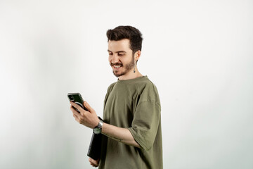 Young man wearing khaki t-shirt posing isolated over white background holding in hands carrying laptop and phone posing. Looking at the phone screen.