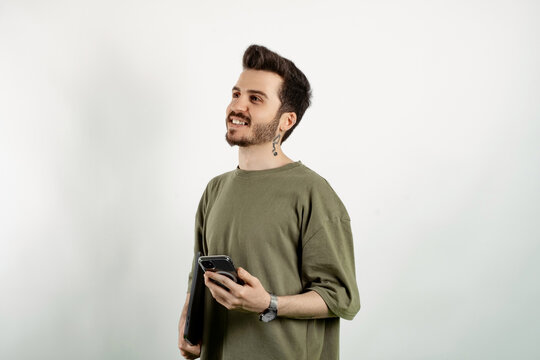 Handsome caucasian man wearing khaki t-shirt posing isolated over white background holding in hands carrying laptop and phone posing. Looking away.