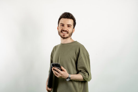 Cheerful caucasian man wearing casual clothes posing isolated over white background holding in hands carrying laptop and phone posing. Looking at the camera with big smiles.