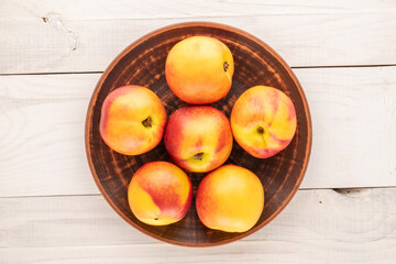 Several ripe juicy nectarines with a ceramic dish on a wooden table, close-up, top view.