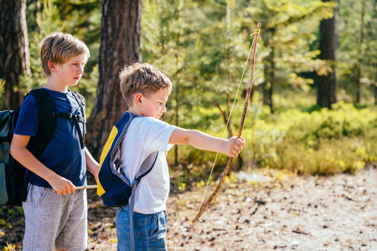 Sunny Summer Day. Cute little boy with his brother shooting with a hand made bow and arrow in forest. Summer vacation. Archery. Outdoor activities for kids.
