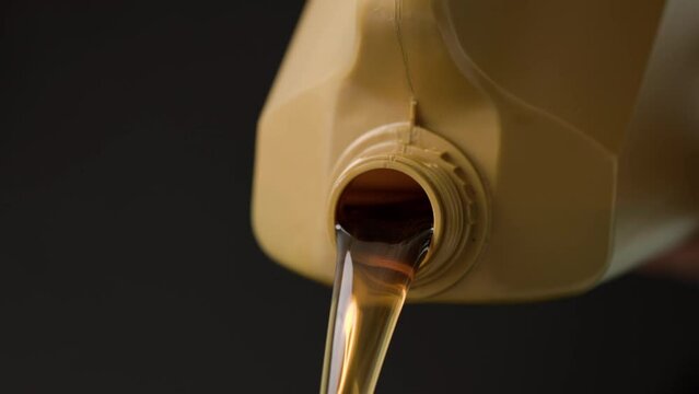 pouring motor oil from the golden plastic canister on black background. slow-motion close-up pouring engine oil in black background.