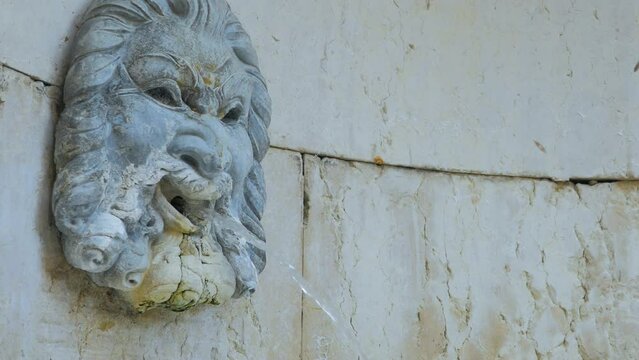 Roman marble face fountain.
Close up of an ancient italian fountain whose jet of water flows from the mouth. Medieval sculpture of Neptune's face with open mouth.