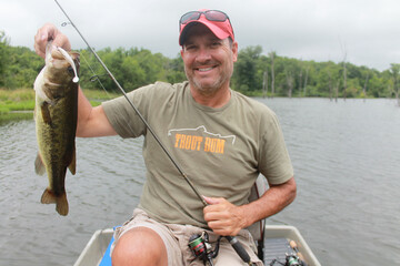 An angler with a largemouth bass caught while fishing from a small boat 