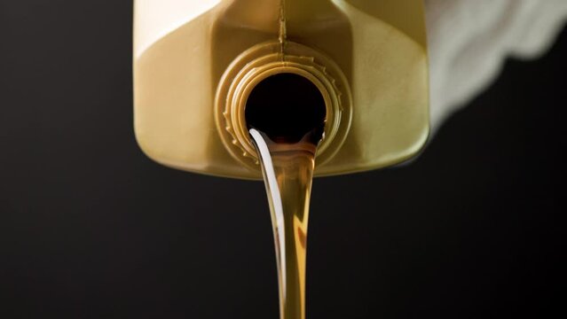 pouring motor oil from the golden plastic canister on black background. slow-motion close-up pouring engine oil in black background.