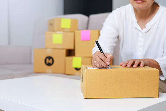 Entrepreneurs are packing boxes at home, Small business selling ideas for sme, Pack products to send to customers, woman writing something on paper, home delivery concept.