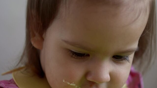 Close up of dirty Face lovely baby girl kid eating have breakfast eggs vegetables sausage by herself at home. Adorable possitive happy toddler child eats at table indoor. Food, nutrition healthy life