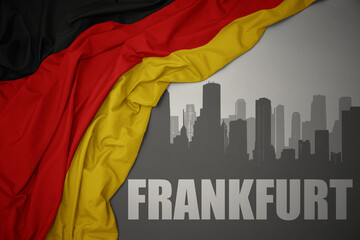 abstract silhouette of the city with text Frankfurt near waving national flag of germany on a gray background.