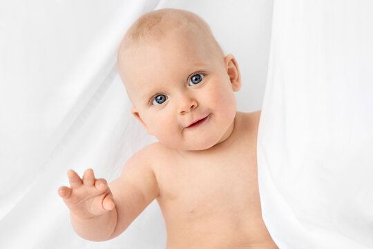 Portrait of blue-eyed baby peeking behind white sheet
