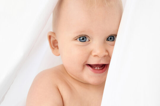 Close-up portrait of blue-eyed baby peeking behind white sheet
