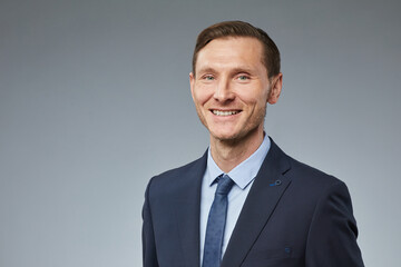 Portrait of smiling adult businessman looking at camera against plain grey background, copy space