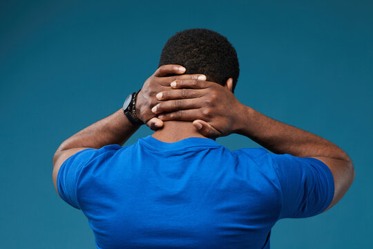Back view of muscular black man with hands on neck wearing blue against vibrant blue background