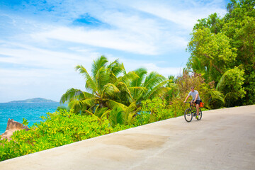 Happy young guy riding a bike on the road by the sea in the Seychelles. Concept of vacation and...