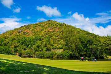 Obraz premium Golfers drive a golf car across a golf course in the Seychelles. Golf sport in the background of a tropical landscape.