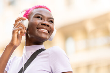 Smiling afro woman using headphones on the street