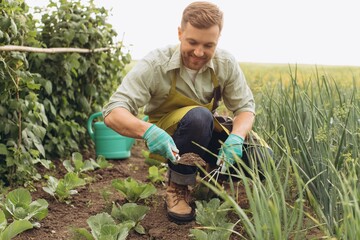 Happy farmer man waters the beds and works in the garden