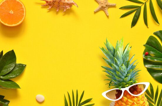 Summer background. Palm leaf, pineapple in sunglasses, starfish and seashell on yellow background.