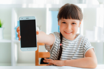 child or a teenage girl is smiling, holding a smartphone or mobile phone for show, showing an empty...