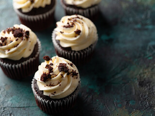 Top view of chocolate muffins topped with cream and sprinkled with grated dark chocolate on a green marble background. Holiday, birthday, delicious dessert. Banner, advertisement, invitation.