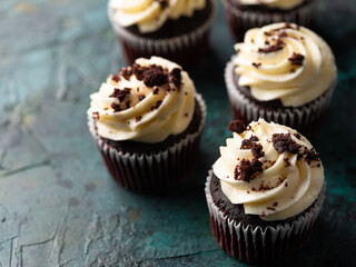 Chocolate cupcakes with whipped cream garnished with grated dark chocolate on a green marble background. Close-up. Lots of objects. There are no people in the photo.