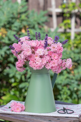 romantischer Blumenstrauß mit pink Rosen und Lavendel im vintage Krug im Garten