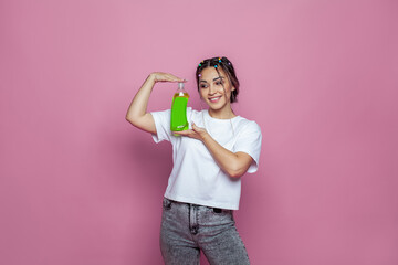 Cheerful young woman showing plastic bottle against pink studio wall background