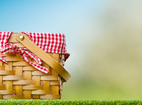 Against the backdrop of a light blue sky, a straw picnic basket on green grass. Summer holidays, walks, romance, family holidays, holidays with friends. Banner, invitation, postcard.