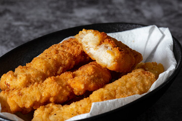 Breaded chicken fillet strips on a paper towel in a black bowl. On a concrete background