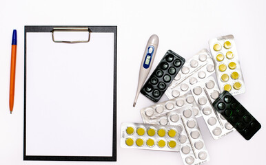 A universal tablet, a notebook for writing a prescription by a doctor, a medical thermometer and medicines on the table.
