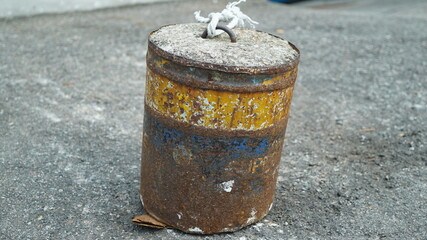 Naklejka premium A rusty barrel full of cement on asphalt