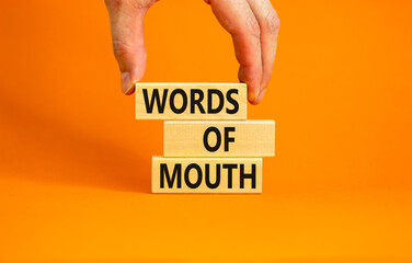 Words of mouth symbol. Concept words Words of mouth on wooden blocks on a beautiful orange table orange background. Businessman hand. Business, finacial and words of mouth concept. Copy space.