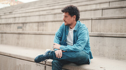 Upset man sits on the stairs and thinks emotionally. Closeup portrait of emotional young bearded...