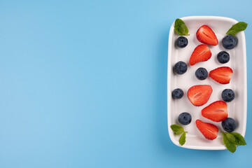 Plate with berries and mint leaves on a blue background, template for inserting text, menu, copy space 