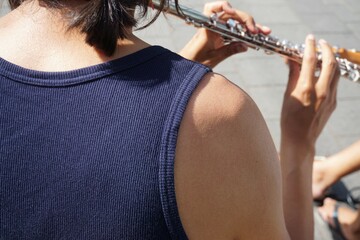 Musiker mit blauem ärmellosen Rippshirt spielt Querflöte auf Straße bei Sonne am Nachmittag im...