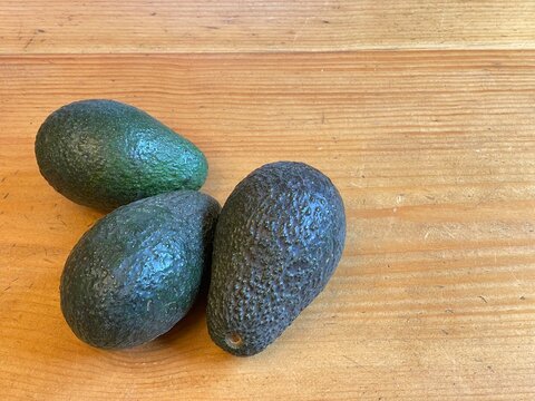 Three avocados on a wood surface