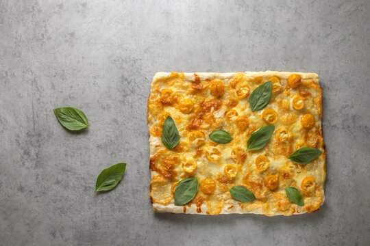 square homemade pizza with mozzarella, orange tomatoes and basil, on a concrete background, copy space