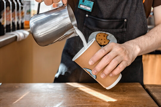a barista in an outdoor cafe pours coffee into a paper cup
