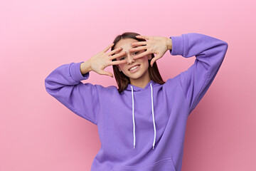 a joyful, happy woman stands on a pink background in a purple tracksuit and covers her face with her hands