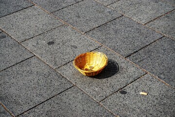 Kleines braunes Flechtkörbchen mit Geldmünzen auf Straße in Stadt bei Sonne im Frühling 