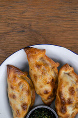 Traditional Argentinian food. Top view of empanadas with chimichurri dipping sauce, in a white bowl on the wooden table. 